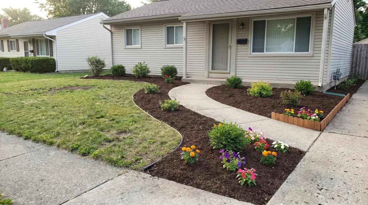 Simple ranch home with fresh curved mulch beds, annual flowers and a concrete path