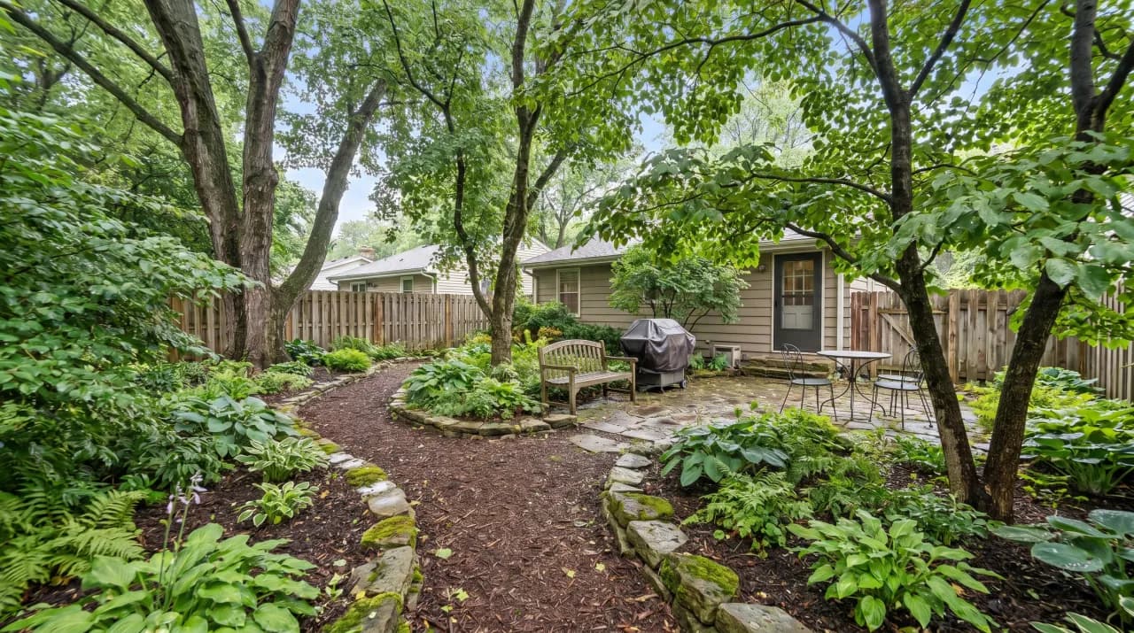 Shaded backyard with winding stone path through hostas, ferns and mature trees with a garden bench